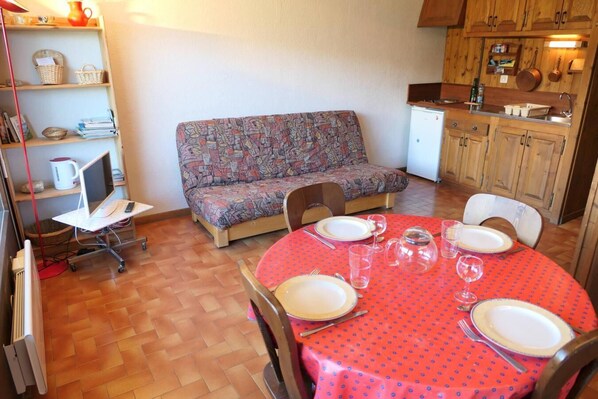 Een gezellig, compact leefruimte met een bank, een eettafel gedekt voor vier personen en een kitchenette.