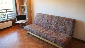 A small room with a sofa, a desk with a computer, and a window with a view of buildings. - 300m from ski slopes, 1st floor, view mountain, balcony, parking, tv, 28m², Saint Gervais (Saint-Gervais-les-Bains)
