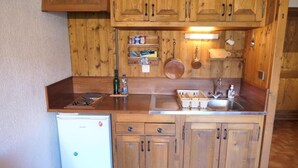 A compact kitchen with wooden cabinets, a built-in stove, a sink, and a refrigerator. - 300m from ski slopes, 1st floor, view mountain, balcony, parking, tv, 28m², Saint Gervais (Saint-Gervais-les-Bains)