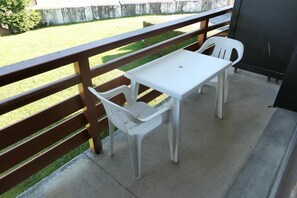 Een balkon met een witte tafel en twee witte stoelen.