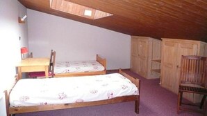 Une petite chambre mansardée, chaleureuse et accueillante, avec deux lits en bois, un bureau et une chaise.