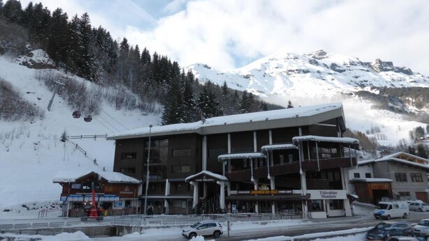 A multi-story building with a ski lift in the background, surrounded by snow-covered mountains.