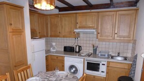 A compact kitchen with wooden cabinets, a washing machine, a microwave, and a sink.
