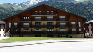 A multi-story wooden building with balconies, set against a mountainous backdrop.