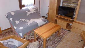 A small room with a bed, a wooden bench, a television on a wooden stand, and a patterned rug.