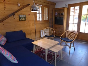 Un cuarto acogedor con un sofá azul, dos sillas de mimbre, una mesita de madera y una lámpara colgante.