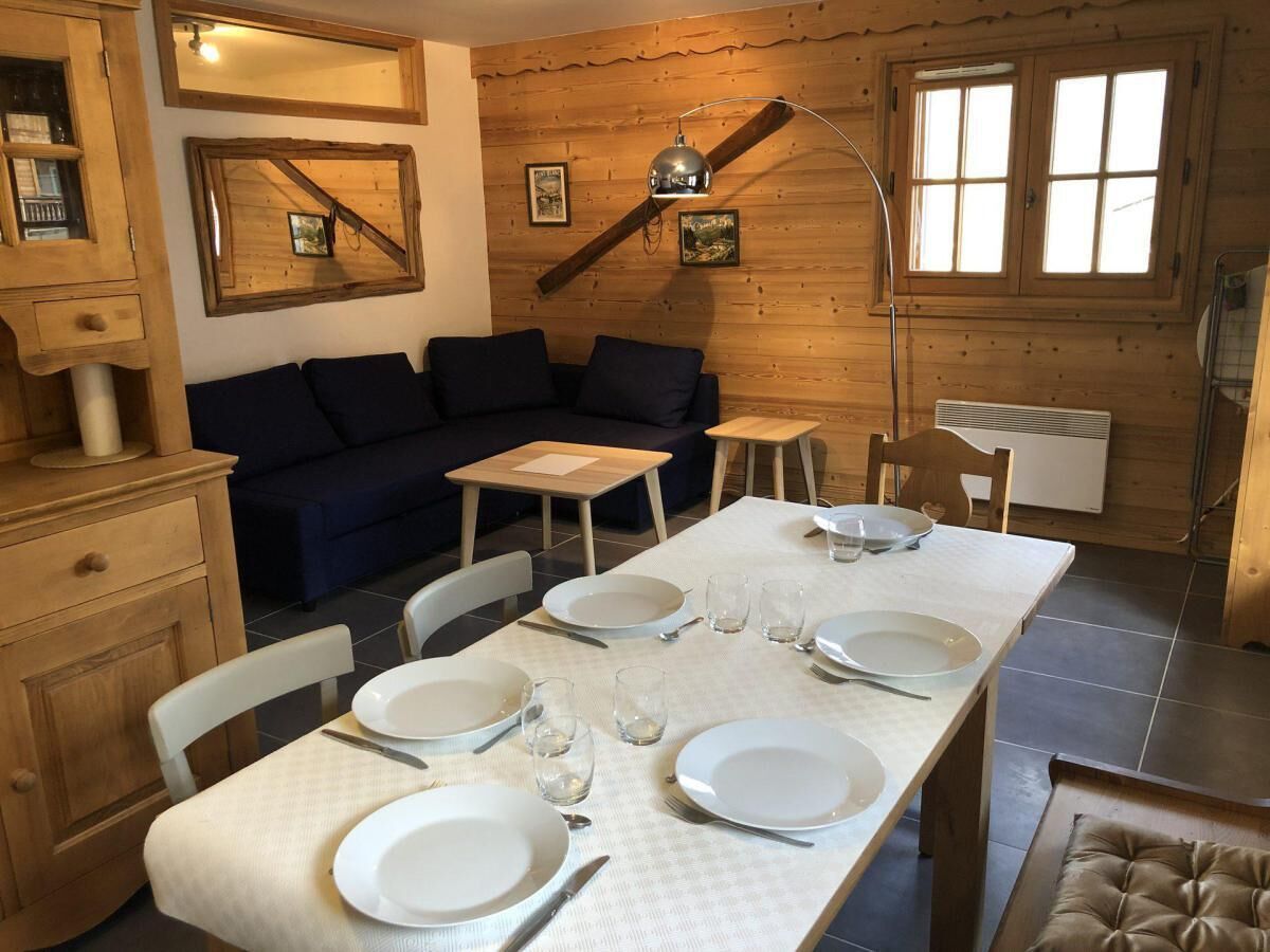 Un comedor con una mesa larga dispuesta para cuatro, paredes de madera, un sofá y una lámpara.