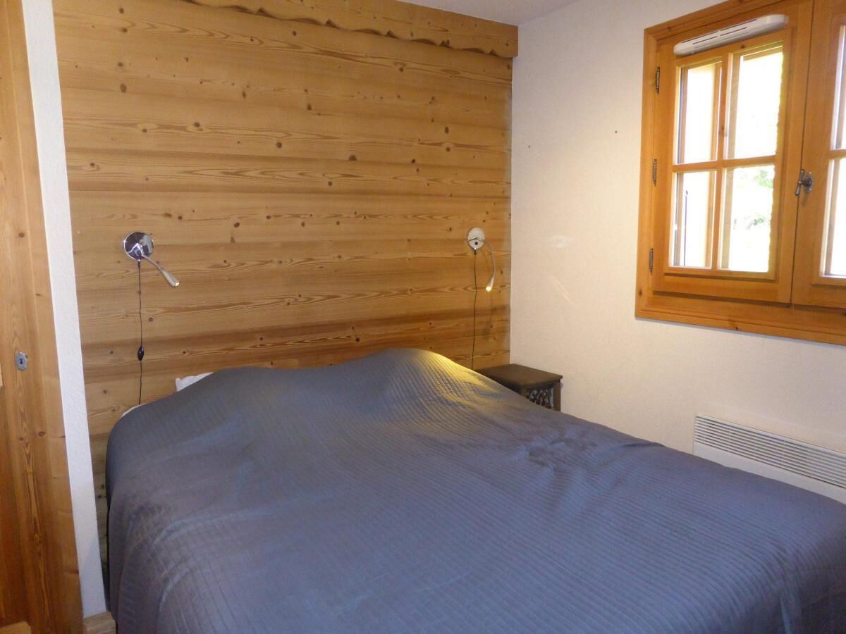 A bedroom with a wooden ceiling, a bed with a grey bedspread, a small bedside table, and a window with wooden shutters.