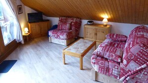 A cozy attic room with wooden flooring, a wooden ceiling, and a red patterned sofa set. - 200m from ski slopes, 3rd floor, view mountain, balcony, parking, tv, ski locker, 38m² (Les Contamines-Montjoie)