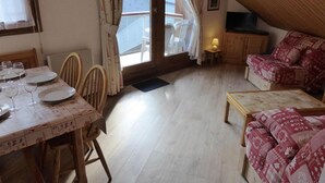 A cozy room with a dining table set for four, a sofa, and a small wooden cabinet. - 200m from ski slopes, 3rd floor, view mountain, balcony, parking, tv, ski locker, 38m² (Les Contamines-Montjoie)