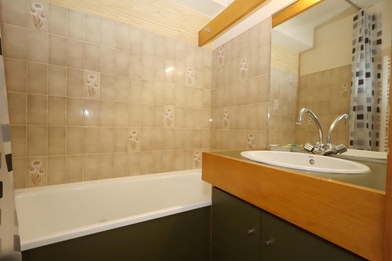 A bathroom with a bathtub, a sink with a mirror, and beige tiled walls with floral patterns.