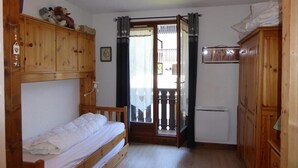Una habitación pequeña y acogedora con una cama nido, un armario de madera, un refrigerador compacto y un balcón con vistas.