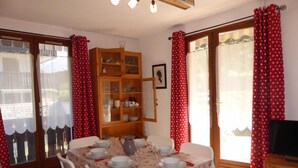 Un comedor con una mesa dispuesta para cuatro, un armario de madera con vajilla, y un televisor sobre un mueble.