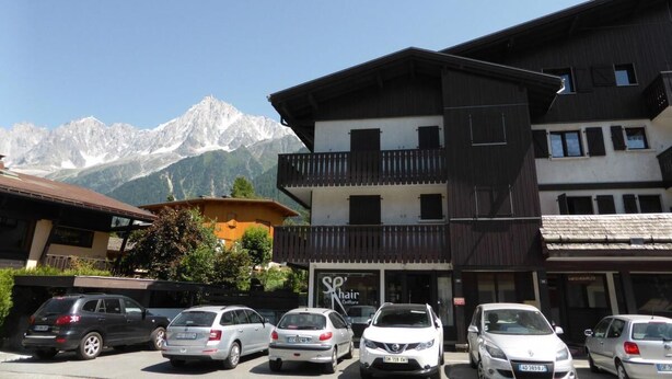 Un hotel con vista a la montaña, un estacionamiento con varios coches y un cartel que dice 'Hair Salon'.