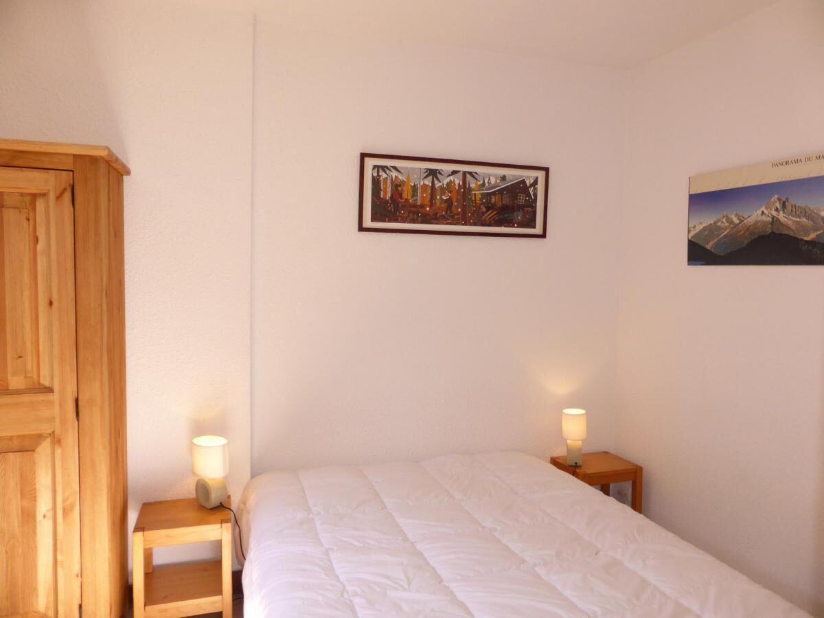 A bedroom with a bed, two bedside tables with lamps, a wooden wardrobe, and two framed pictures on the wall.