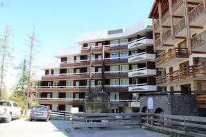 Un hotel a più piani con balconi, una facciata in pietra e un'area di parcheggio con auto.