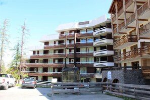 A multi-story hotel with balconies, a stone facade, and a parking area with cars.