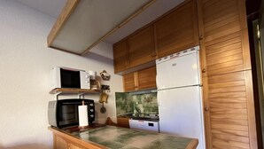 A compact kitchen with wooden cabinets, a microwave, a refrigerator, and a tiled countertop.