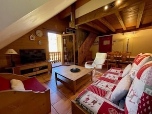 Un salon chaleureux avec un plafond en bois, une télévision, un canapé et une table à manger.