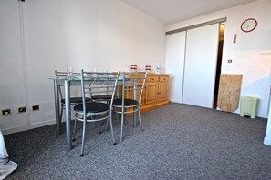 A room with a glass-top table and two chairs, a wooden cabinet, a clock on the wall, and a sliding door.