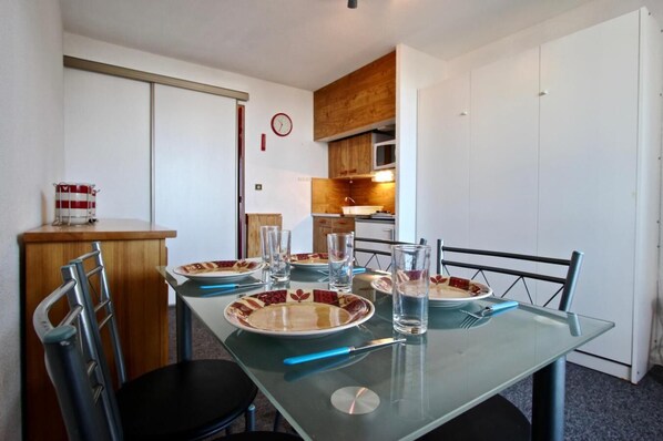 A dining area with a glass table set for four, chairs, and a kitchen in the background. - 4th floor, balcony, tv, ski locker, 21m², Chamrousse (Chamrousse)