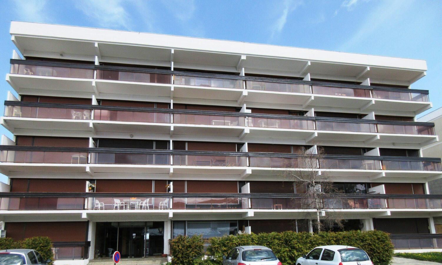 Un edificio de varios pisos con balcones, zona de estacionamiento y cielo despejado.