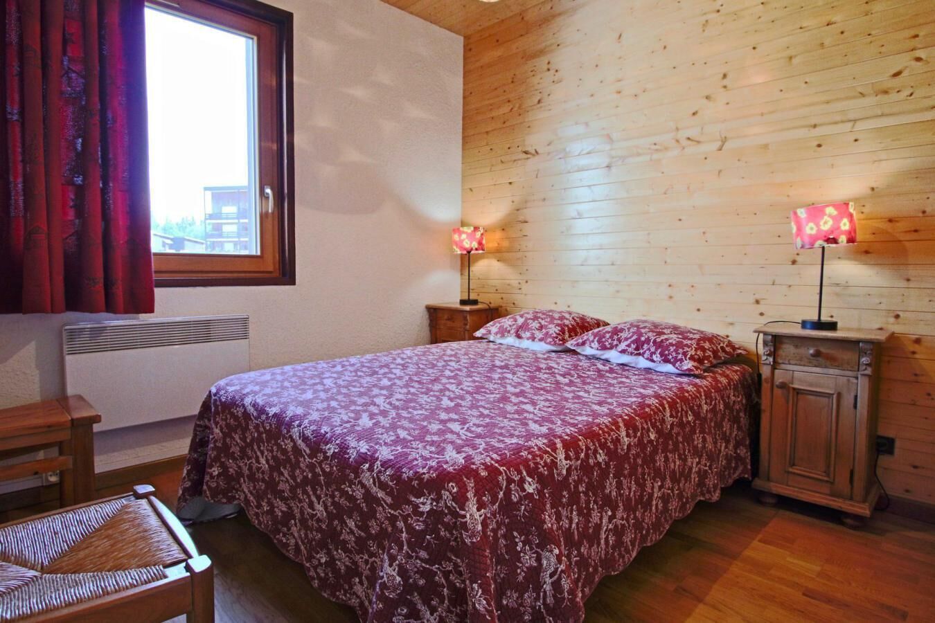 Une chambre à coucher avec un grand lit, deux lampes de chevet, une armoire en bois et une fenêtre avec des rideaux.