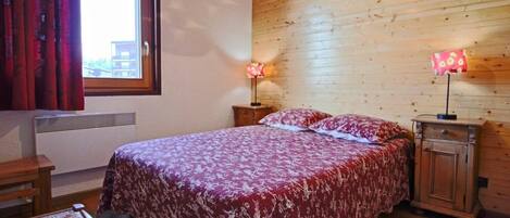 Une chambre à coucher avec un grand lit, deux lampes de chevet, une armoire en bois et une fenêtre avec des rideaux.