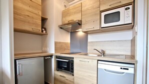 Une cuisine compacte dotée d’un micro-ondes, d’un four et d’un lave-vaisselle intégrés, avec des meubles en bois et un évier en acier inoxydable.