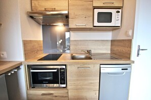 A compact kitchen with a microwave, oven, and dishwasher built into wooden cabinetry. - 20m from resort center, 5th floor, balcony, tv, 30m², Chamrousse (Chamrousse)
