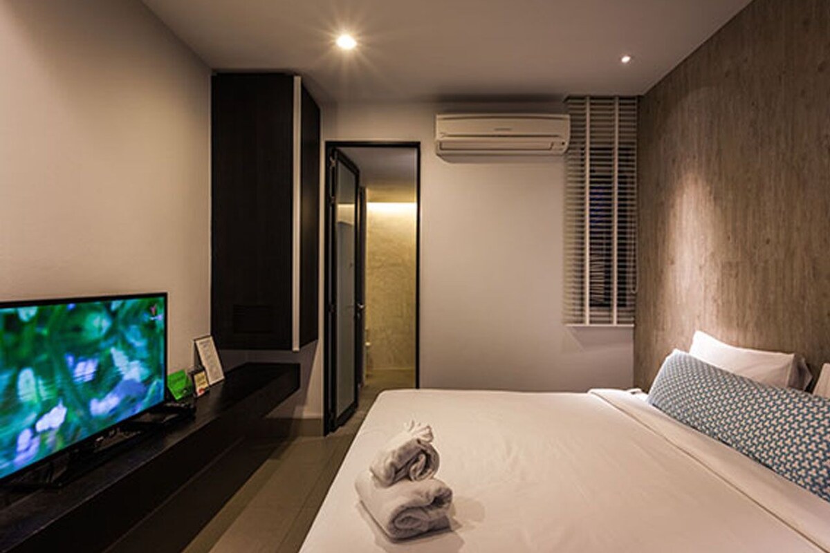 Ein modernes Hotelzimmer mit einem großen Bett, einem Flachbildfernseher, einem dunklen Holzschrank und einer Klimaanlage.