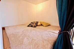 Ein Einzelbett mit gemusterten Betttextilien, einem Kopfkissen und einem Vorhang.