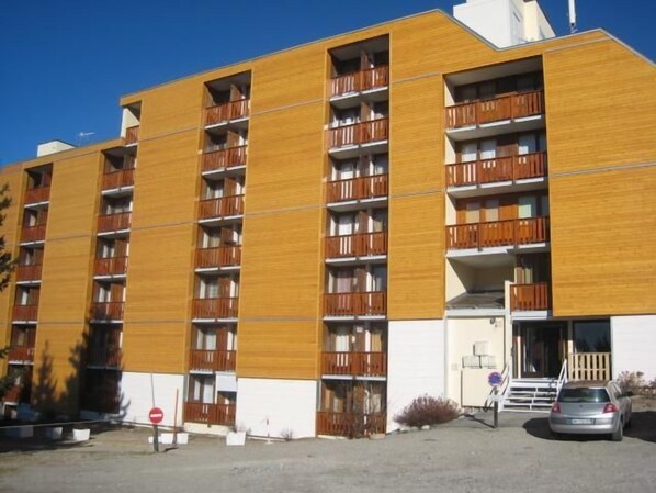 A multi-story building with balconies, a car parked in front, and a no-entry sign.