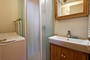 Ein Badezimmer mit Waschmaschine, Dusche und Waschbecken mit Spiegel darüber.