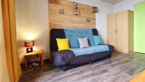 Ein Zimmer mit hölzernem Kopfteil, einer Couch mit Kissen, einem kleinen Tisch mit Lampe und einem Kleiderschrank.