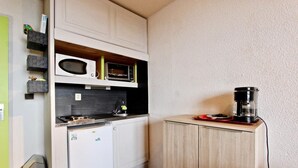 Eine kleine Küche mit Mikrowelle, Herd und Kühlschrank. Eine Kaffeemaschine steht auf einer Holzausziehtisch.