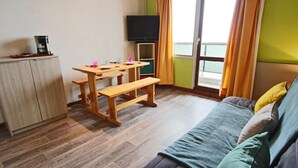 A small, cozy room with a wooden table, a bench, a television, and a sofa.