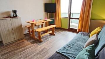 Una habitación pequeña y acogedora con una mesa de madera, un banco, un televisor y un sofá.