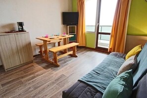 A small, cozy room with a wooden table, a bench, a television, and a sofa.