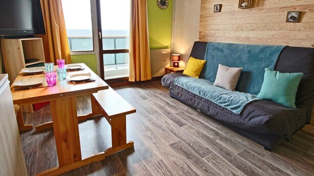 Ein gemütlicher Wohnbereich mit einem Holztisch, der für das Essen gedeckt ist, einer Couch mit Kissen, einem Fernseher und einer Holzwand mit gerahmten Bildern.