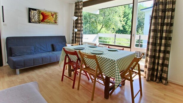 A dining area with a table set for four, a blue sofa, and a painting on the wall. - 150m from ski slopes, 3rd floor, balcony, tv, 25m², Chamrousse (Chamrousse)