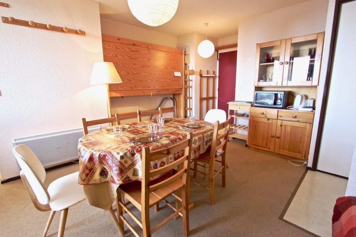Ein Essbereich mit Holztisch und Stühlen, einer Lampe sowie einer Küche mit Holzschränken und Geräten.