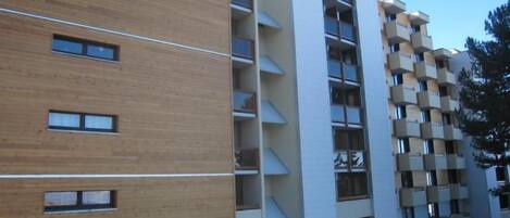 A modern multi-story building with a mix of wooden and white facades, featuring balconies and large windows.