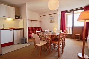 A compact living space with a dining area, kitchenette, and a window with curtains.