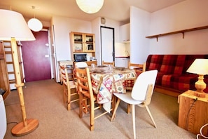A compact living space with a dining table, chairs, a microwave, a cabinet, a sofa, and a lamp.