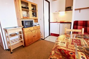 A compact kitchen with a microwave, a small refrigerator, and a wooden cabinet with glass doors.