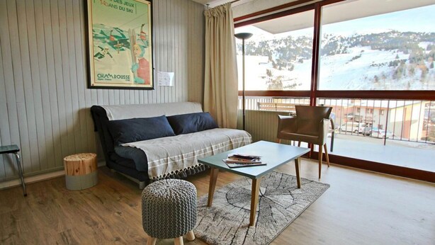Una habitación acogedora con un sofá, una mesita, una silla y vistas a un paisaje nevado a través de un ventanal grande.