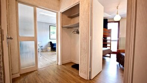 Una habitación con suelo de madera, un armario con perchero y una cama con cabecera.