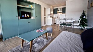 Un espacio habitable compacto con kitchenette, comedor y televisor montado en un mueble azul aguamarina.