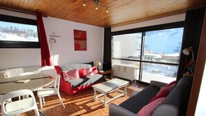Un salon confortable avec un canapé, une table à manger et des chaises. De grandes fenêtres offrent une vue sur l’extérieur.